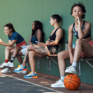 Symbolbild - sportlich gekleidete Jugendliche sitzen auf einer Bank, Basketball im Vordergrund