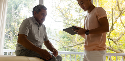 Physiotherapeut untersucht eine Person und verwendet dafür ein Tablet.