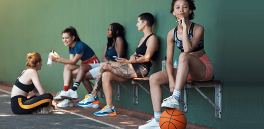 Symbolbild - sportlich gekleidete Jugendliche sitzen auf einer Bank, Basketball im Vordergrund